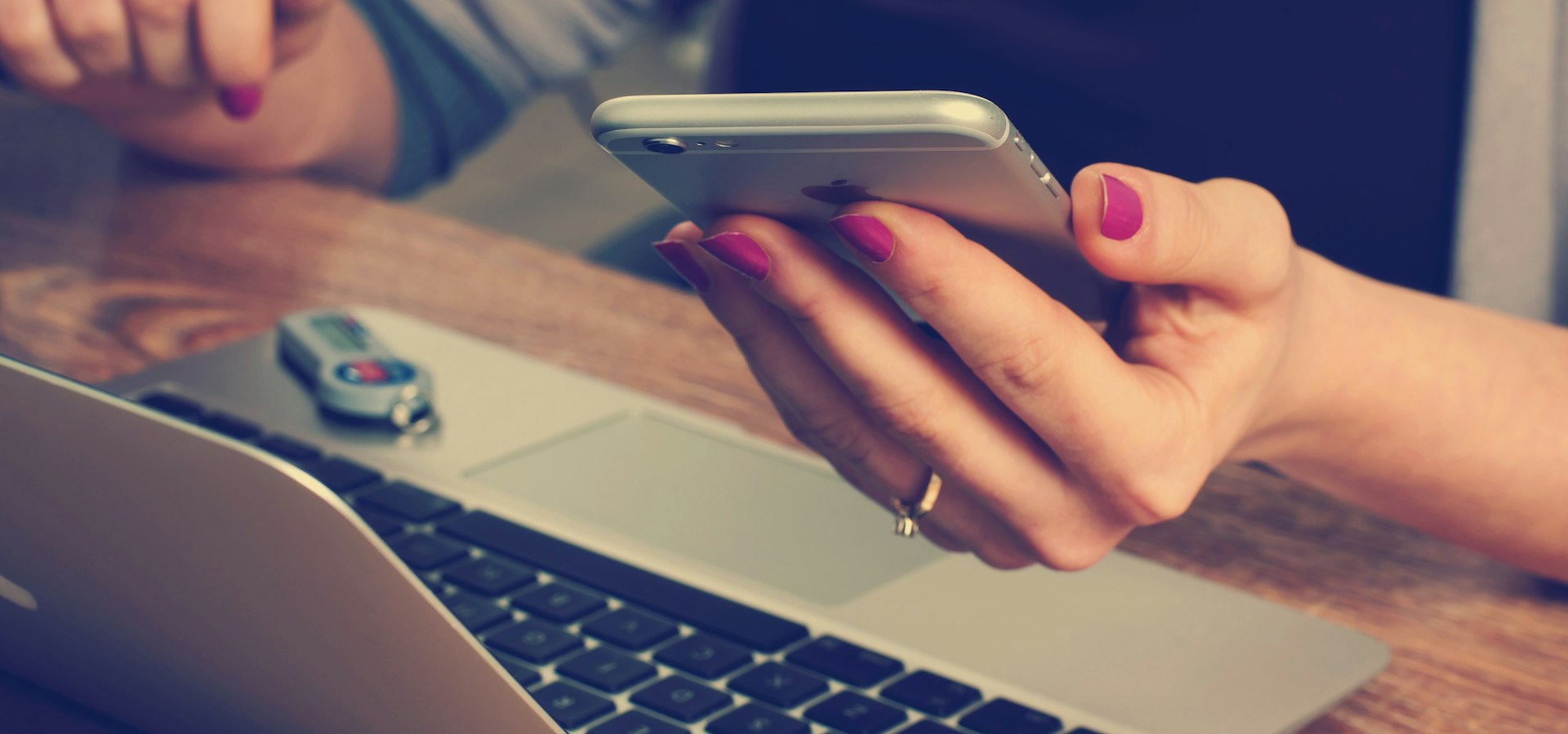 Person am Schreibtisch mit Smartphone und Laptop beim Übermitteln einer Anfrage