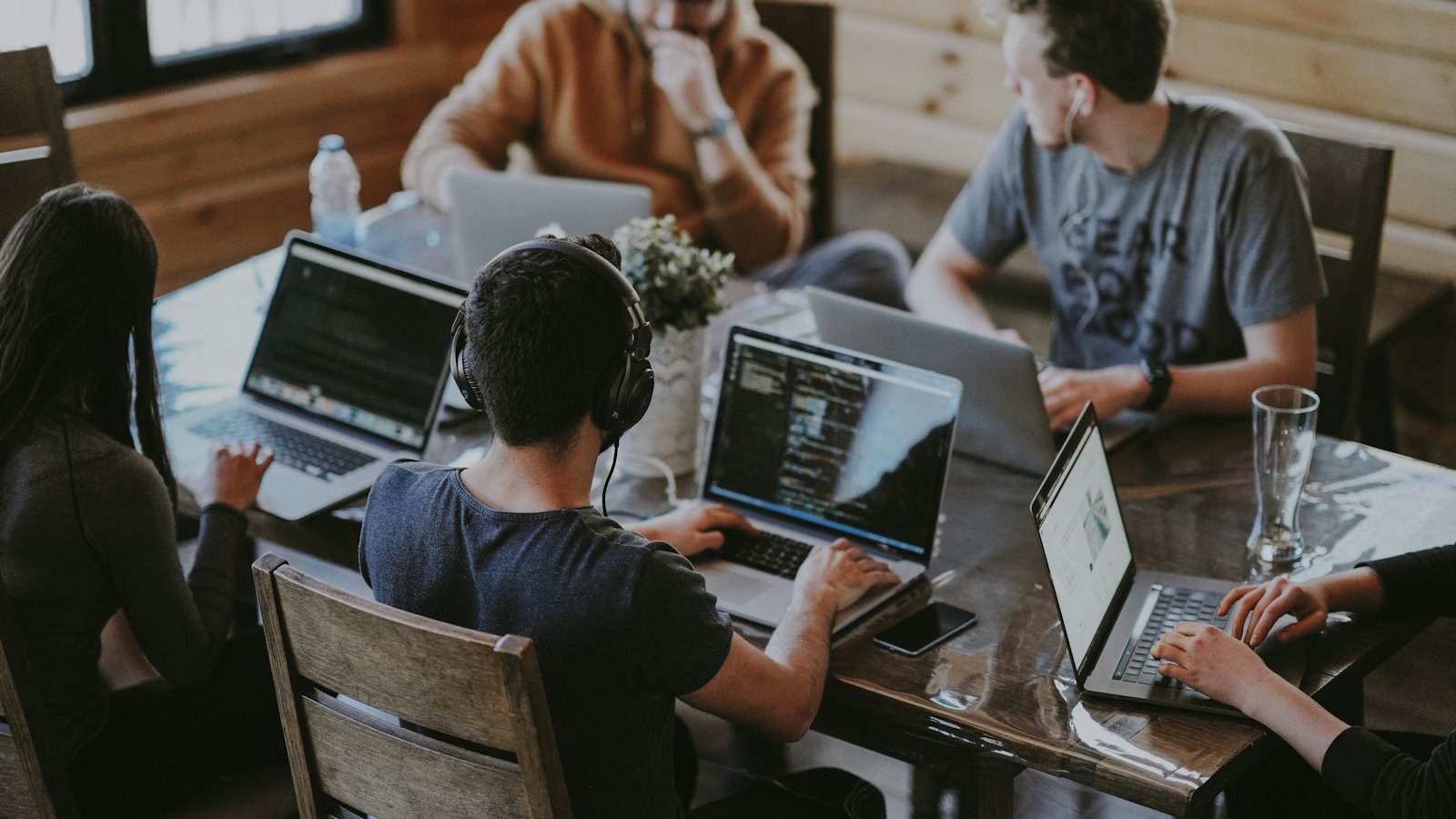 Team arbeitet gemeinsam an Laptops an einem Holztisch – Branchenexperten im Forderungsmanagement