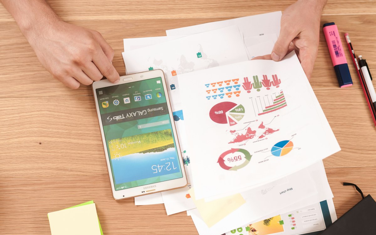 Hände halten Auswertungsunterlagen mit Diagrammen neben einem Tablet – Forderungsanmeldung im Insolvenzverfahren vorbereiten