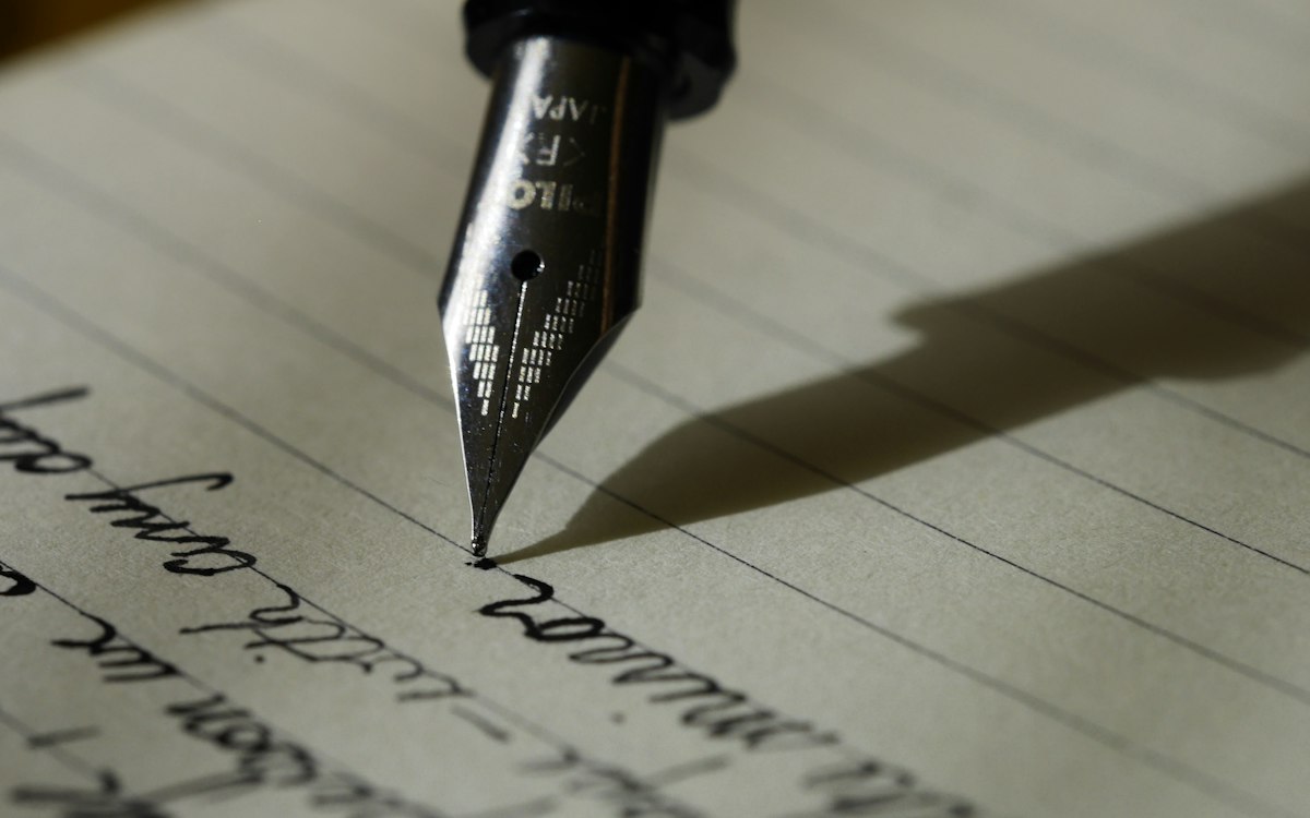 Füllfederhalter schreibt handschriftlich auf liniertes Papier – eine Mahnung sorgfältig formulieren