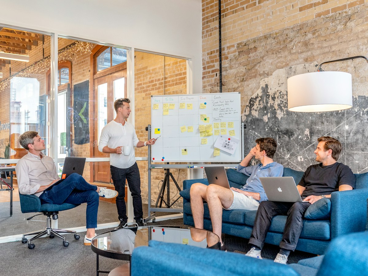 Teammitglied präsentiert am Whiteboard, Kollegen hören im Besprechungsraum zu – gemeinsame Fallbesprechung im Inkassobüro