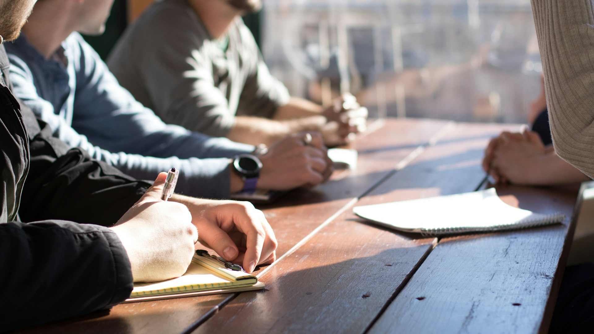 Mitarbeitende machen sich bei einer Besprechung am Holztisch Notizen – das Team von Aurum Inkasso