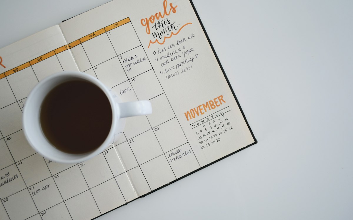 Aufgeschlagener Monatskalender mit Kaffeetasse – Zahlungsfristen und Verzugseintritt im Blick behalten
